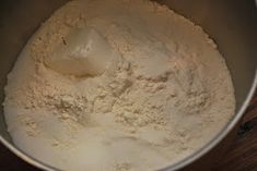 a metal bowl filled with flour on top of a wooden table