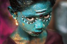 a woman with blue face paint and gold sprinkles on her face is looking at the camera