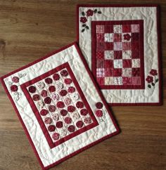 two red and white quilted placemats sitting on top of a wooden table