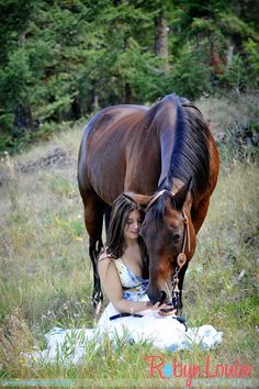 a woman sitting in the grass next to a horse