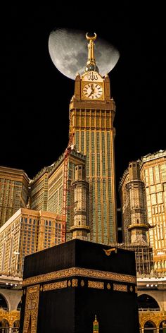 a large building with a clock on it's side in front of the moon