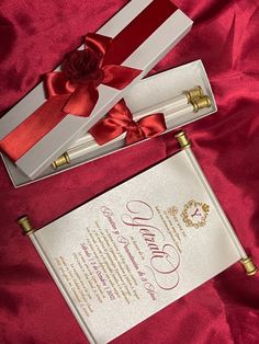 two white boxes with red ribbon and a rose in them on a pink cloth background