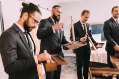 three men in suits are holding wooden boxes and looking at something while another man looks on