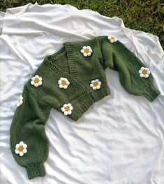 a green sweater with daisies on it laying on the ground next to a white sheet