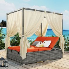 an outdoor daybed with curtains and pillows on the deck next to the ocean,