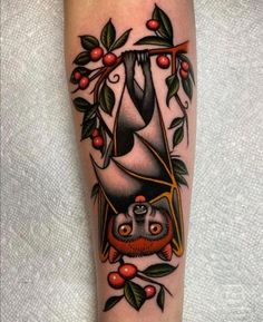 a tattoo with an image of a bat hanging from a tree branch and berries around it