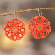 two orange earrings hanging from a tree branch