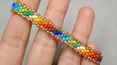 a hand holding a beaded bracelet with multiple colors and gold beads on it's sides