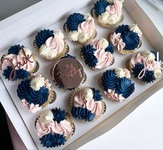 cupcakes with pink and blue frosting in a white box on a table