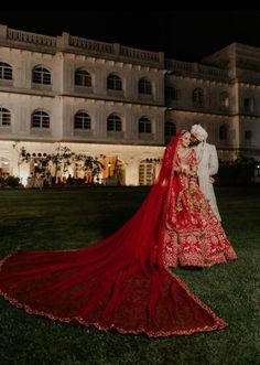 a bride and groom standing in front of a large building at night with their red wedding gown