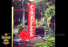 a red sign that says coffee with an arrow pointing to the right in front of some plants and trees