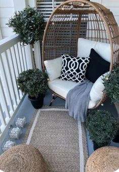 a wicker hanging chair on the front porch with pillows and potted plants next to it