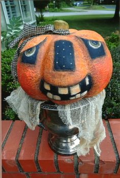 an orange pumpkin sitting on top of a metal pot with a face painted on it