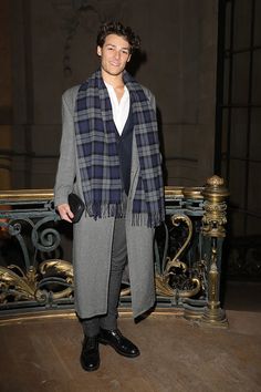 a young man standing in front of a railing wearing a scarf and coat over his shoulders