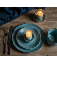 two candles are lit on a blue plate next to a fork, knife and spoon