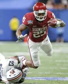 a football player running with the ball in his hand and another person on the ground behind him