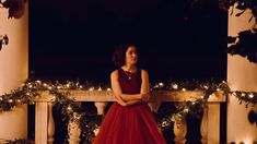 a woman in a red dress is standing on a porch with christmas lights around her