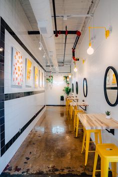 an empty restaurant with yellow stools and wooden tables in the center, along with potted plants on the wall