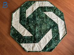 a close up of a green and white quilt on a wooden floor with a circular design