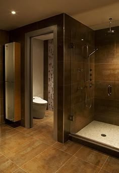 a bathroom with a walk in shower next to a white toilet and brown tiled floor