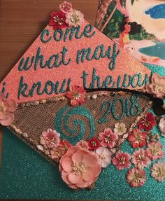 a graduation cap with flowers on it and some other things in the back ground that says, come what may i know they are