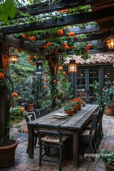 a wooden table surrounded by potted plants and hanging orange flowers on the ceiling above it