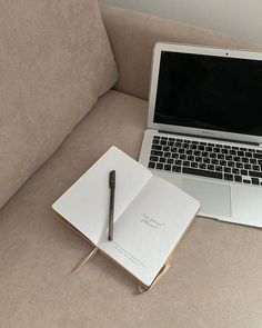 an open notebook and pen sitting on top of a couch next to a laptop computer