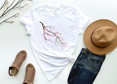 a white t - shirt with a pink flower on it next to some shoes and a hat