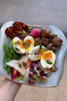 a person holding up a plate of food with hard boiled eggs, meat and vegetables