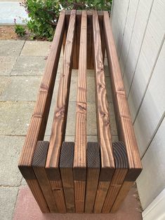 a wooden bench sitting on top of a sidewalk next to a wall and planter