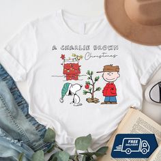 a charlie brown christmas t - shirt on top of a book next to a hat