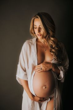 a pregnant woman is holding her belly in front of the camera while wearing a white shirt