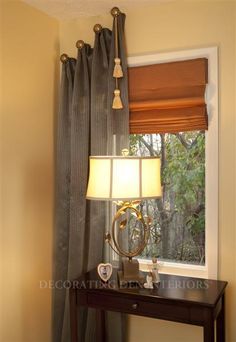 a small table with a lamp on it in front of a window and a curtain