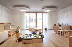 two children playing in a play room with wooden furniture and large windows on the wall