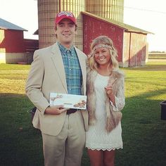 a man and woman standing next to each other in front of a barn with grain silos