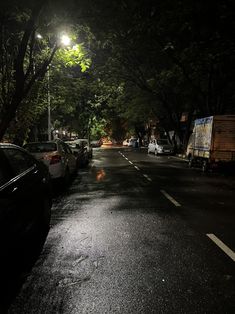 cars parked on the side of a street at night with lights shining in the background