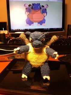 a crocheted stuffed animal sitting on top of a computer desk next to a monitor