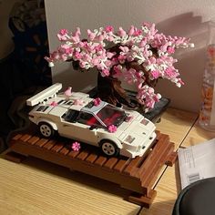 a toy car is parked under a tree with pink flowers on the trunk and in front of it