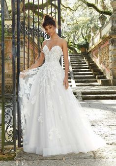 a woman in a white wedding dress standing on steps with an iron gate behind her