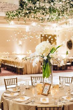 an elegant wedding reception with white flowers and greenery hanging from the ceiling, along with gold tablecloths