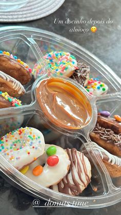 a plastic container filled with lots of different types of doughnuts on top of a table