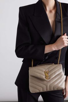 a woman wearing a black blazer and holding a beige handbag with a gold y on it