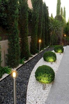 an outdoor garden with gravel and lights in the center, surrounded by trees on either side