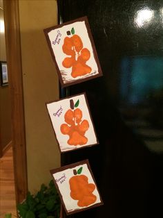 three cards are hanging on the side of a black refrigerator in front of a potted plant