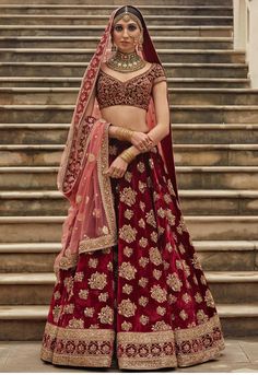 a woman in a red and gold bridal gown standing on steps with her hands behind her head