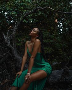 a woman in a green dress is sitting on a tree branch with her eyes closed