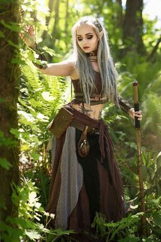 a woman with white hair wearing a costume and holding a staff in the woods,