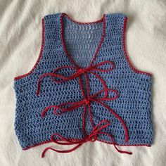 a blue crocheted top with red laces on the front and back, sitting on a white sheet