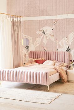 a pink bed with two birds painted on the wall above it and curtains behind it