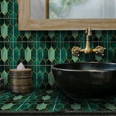 a black bowl sink sitting on top of a green tiled bathroom counter next to a mirror